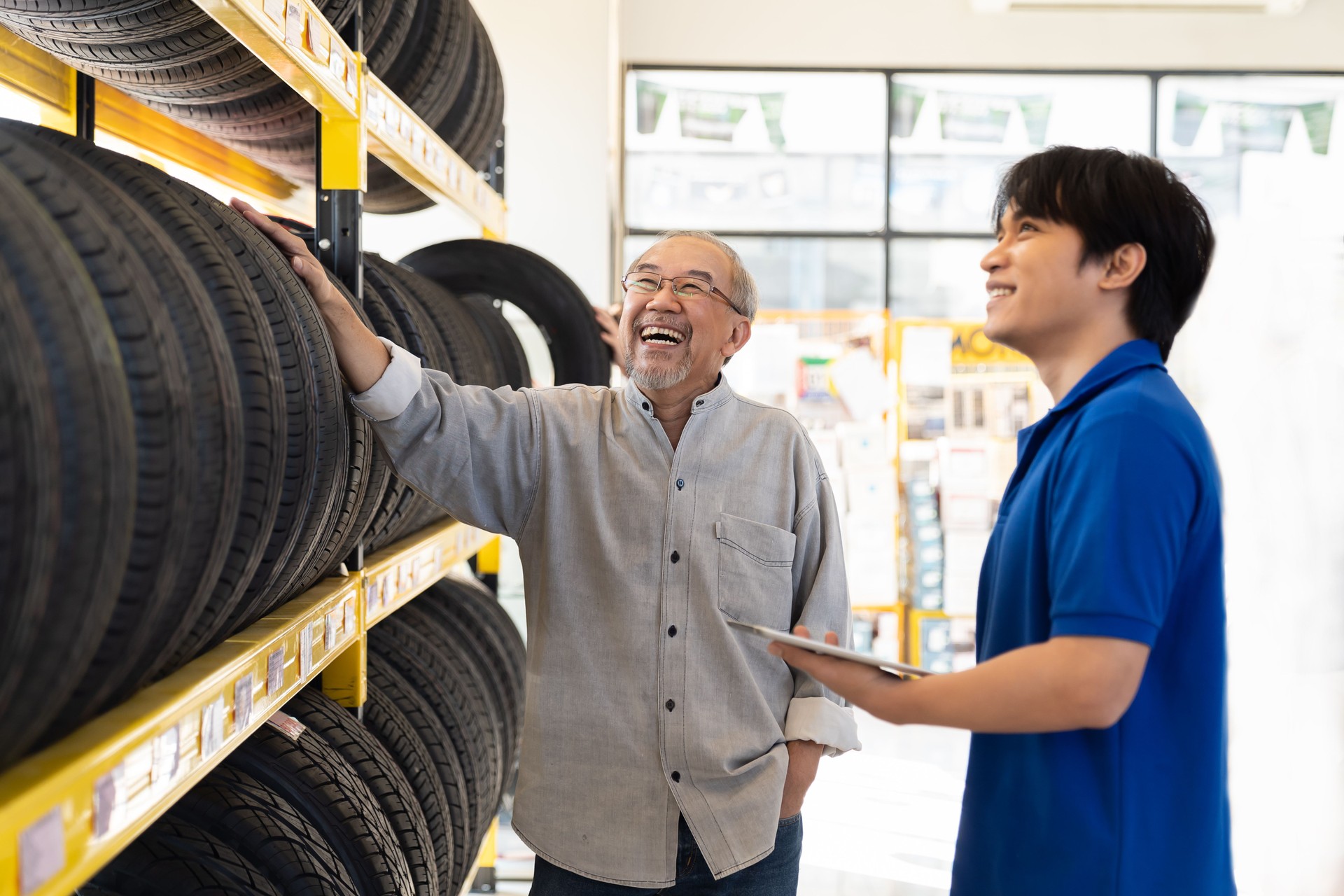 Car service. Asian salesman recommend new tire wheel on shelves shelf to senior elderly customer at the auto car repair shop. Specialist mechanic and customer examining new tire wheel