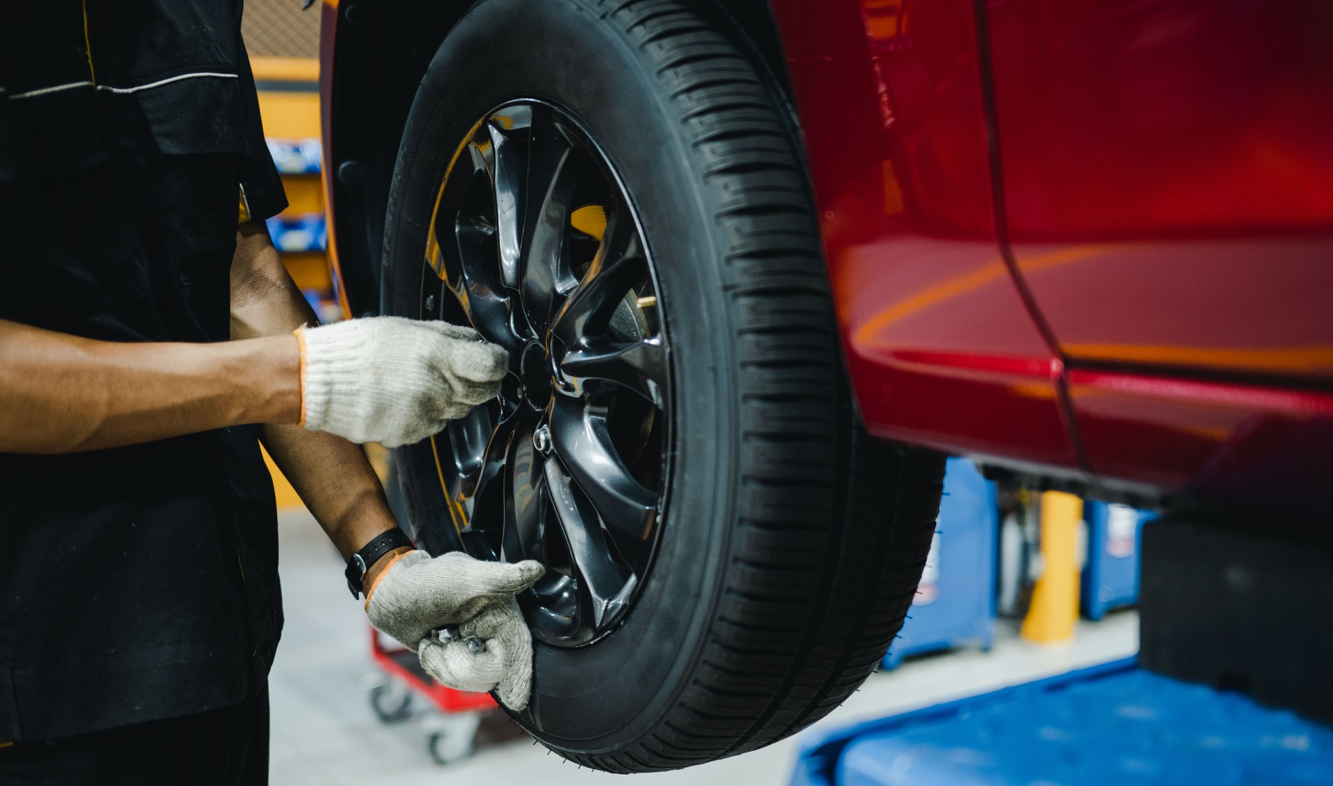 Mechanic with screwdriver repairing car wheel in workshop. Hands replace tires on wheels.