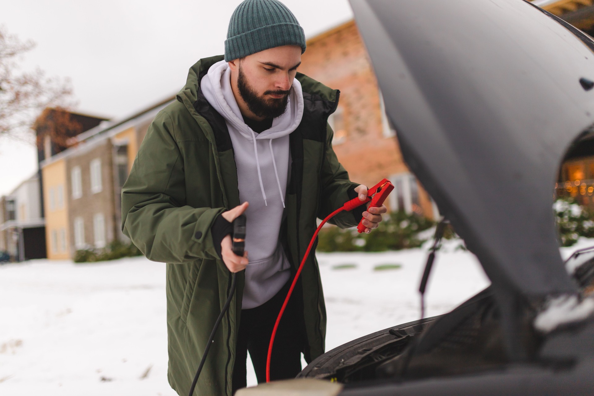 Young man using battery cables to jump start his car in the winter