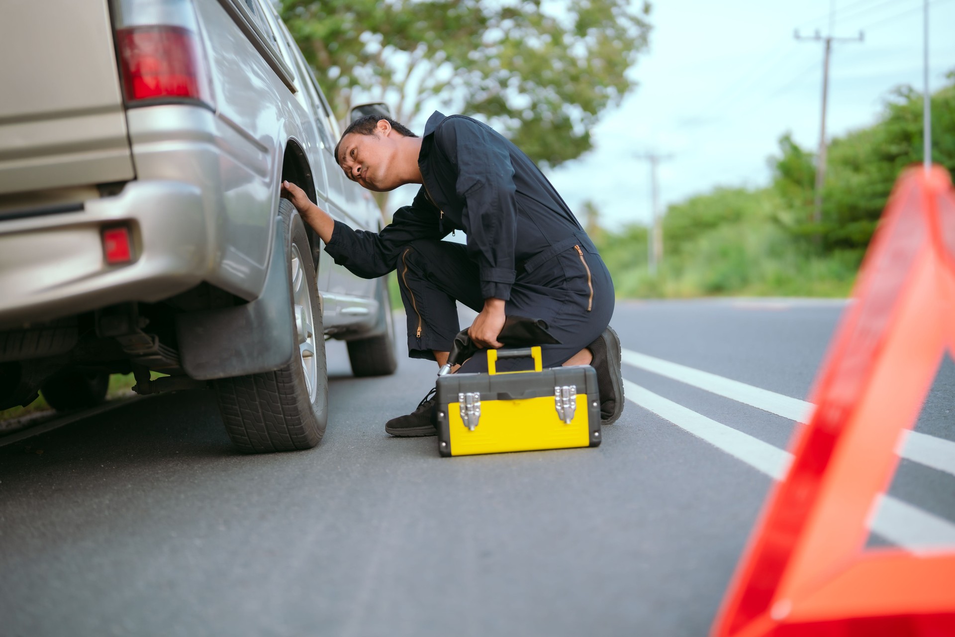 Mechanic checks tire of a stranded vehicle on a rural road during late afternoon