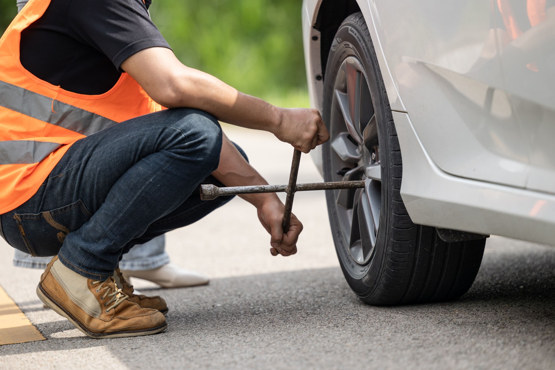 Mechanic team working road assistant help to replace flat tire service at roadside with safety reflective clothes.